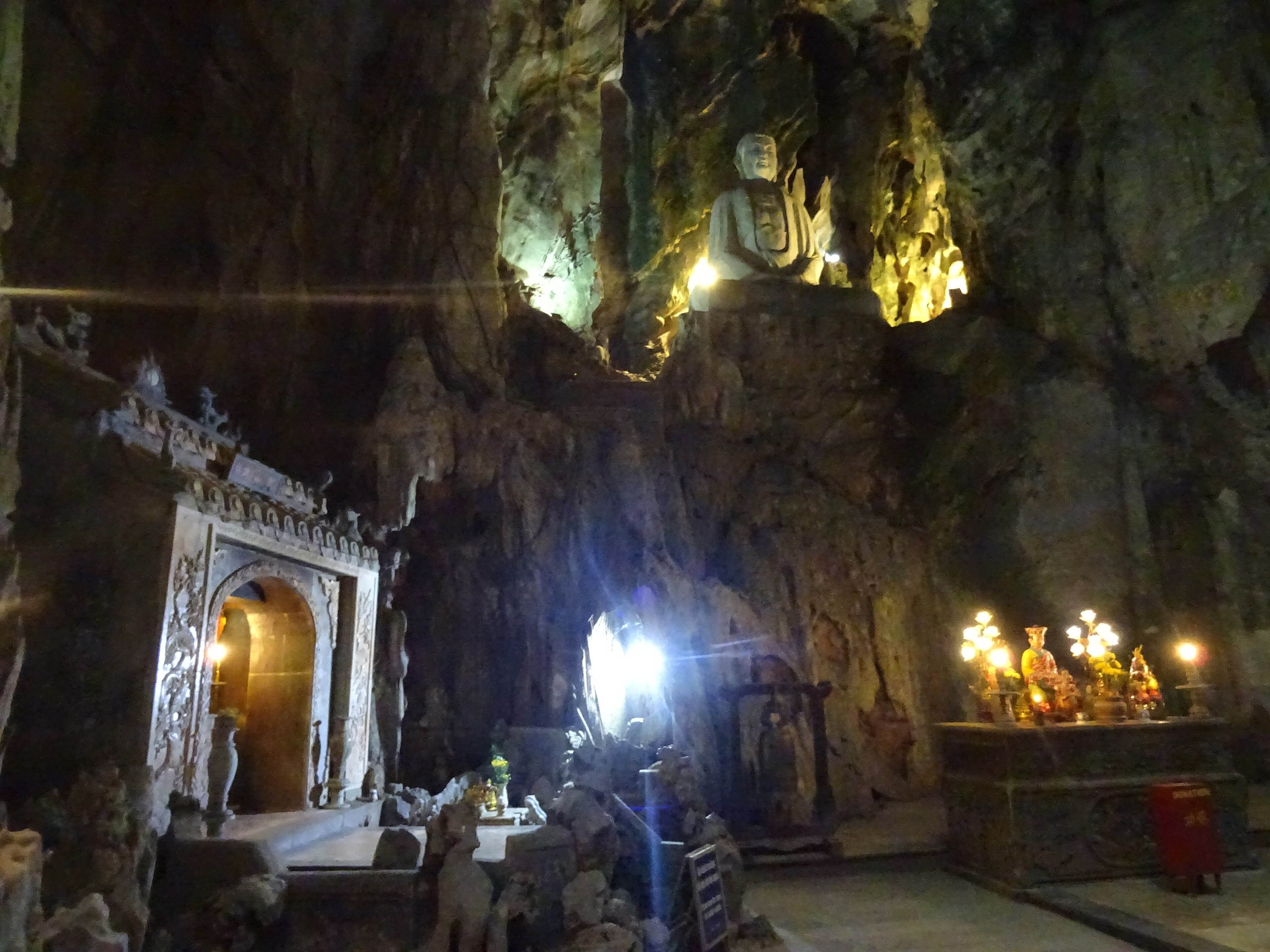 Inside Huyền Không cave: a Buddha carved high in the rock wall above shrines and altars