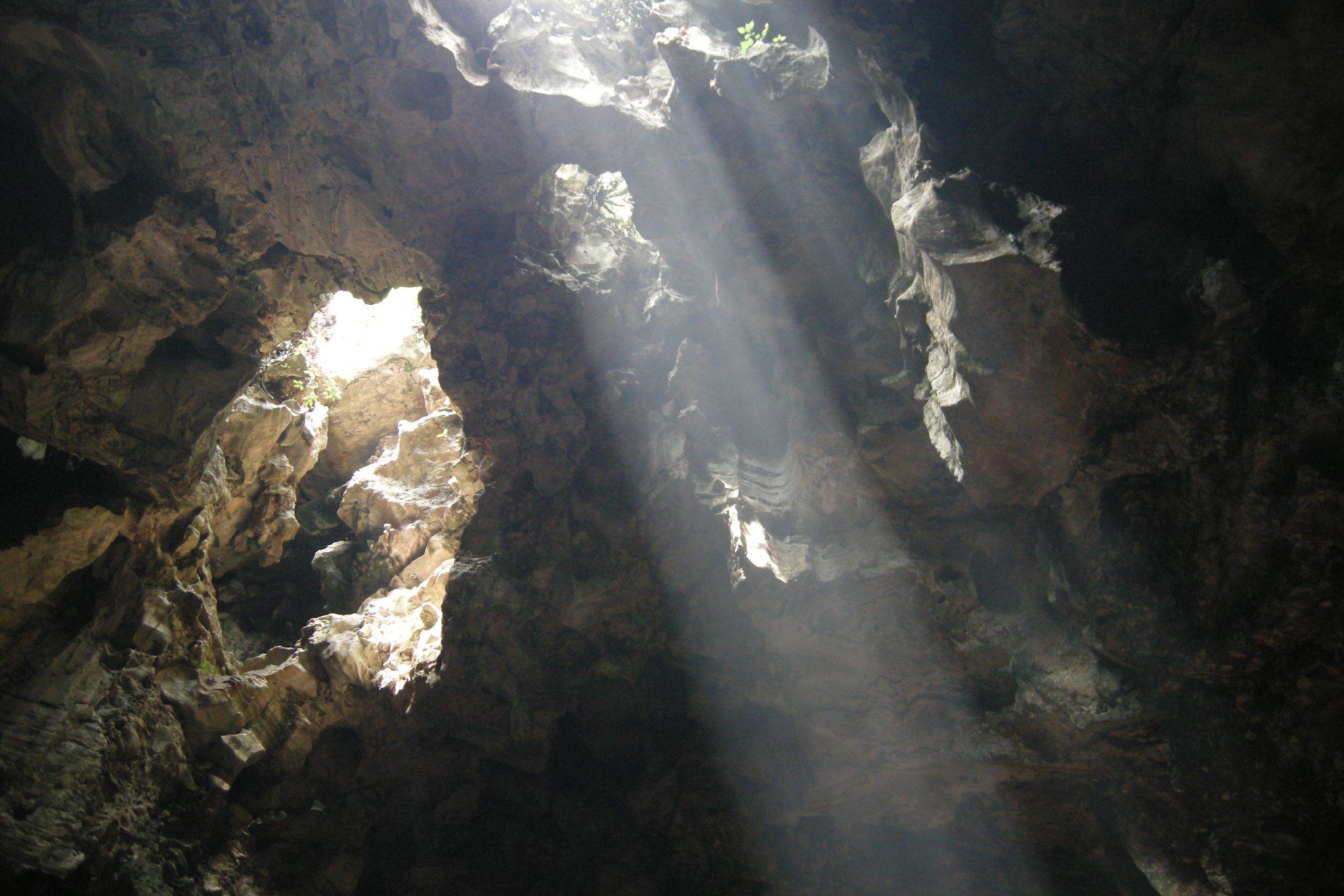 Shafts of sunlight falling through openings in the roof of Huyền Không cave